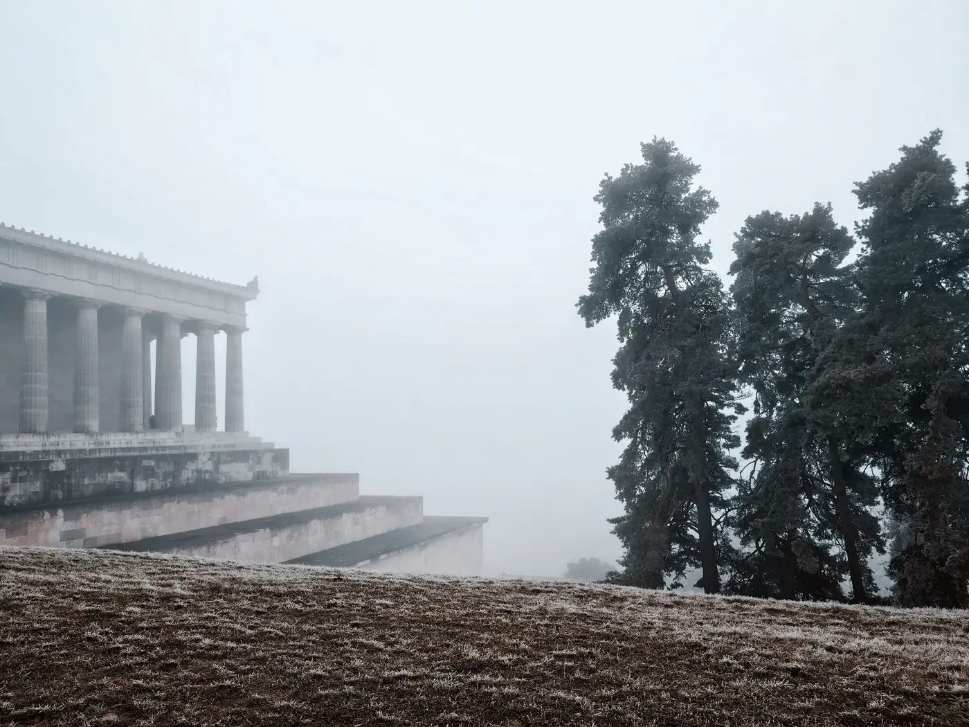 Misty morning scene of Walhalla temple, Bavaria, with fog-shrouded columns and trees.