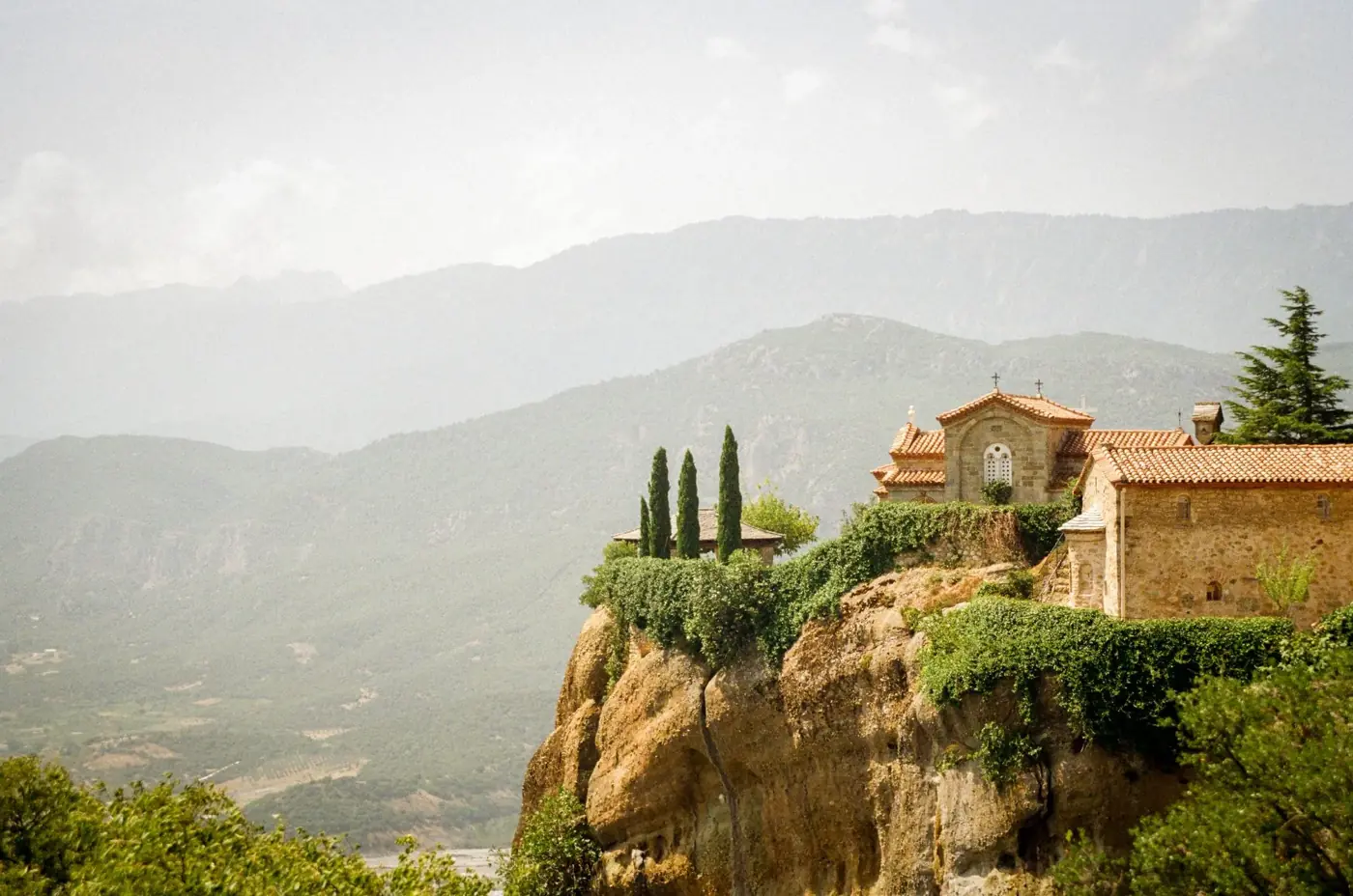 Picturesque monastery perched on a dramatic cliff with mountain backdrop.