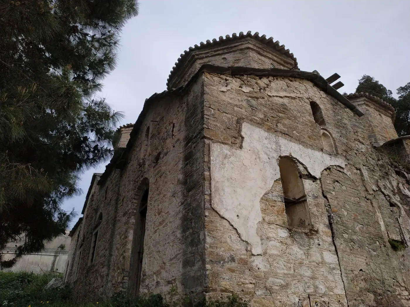Low-angle view of an ancient stone building in Samos, Greece, surrounded by greenery.
