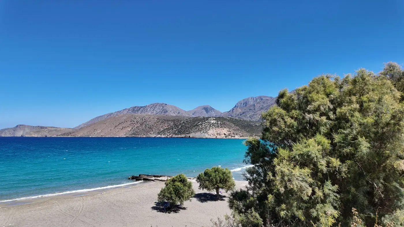 Serene beach in Pacheia Ammos, Greece with turquoise waters and scenic mountain backdrop under a clear blue sky.