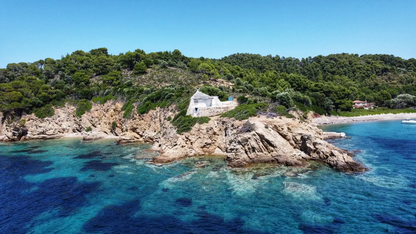 A stunning aerial view of Agios Floros, Greece with clear turquoise waters and lush green landscape.