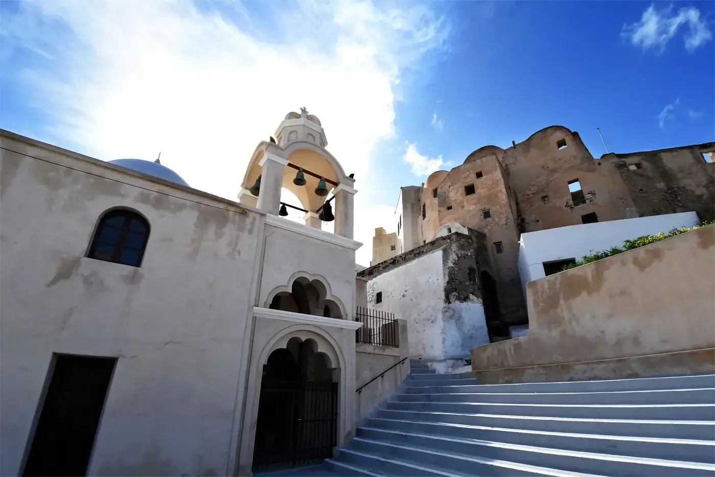 Stunning view of a whitewashed bell tower and steps in Thera, Greece, under a bright blue sky.