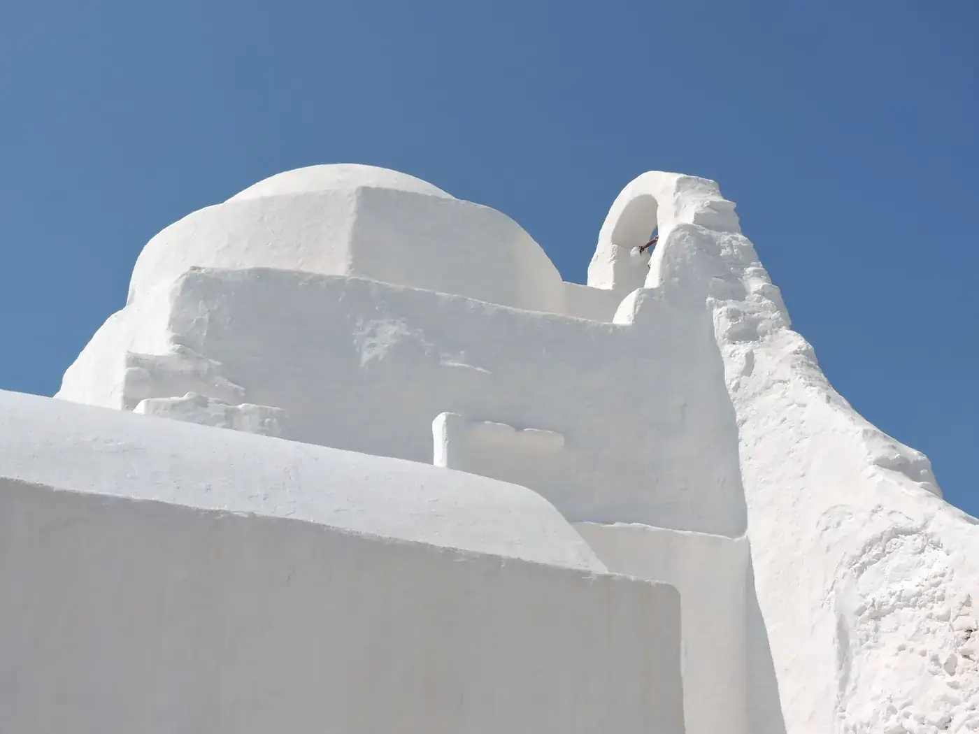 Low-angle view of a traditional whitewashed church in Santorini, Greece, under a clear blue sky.