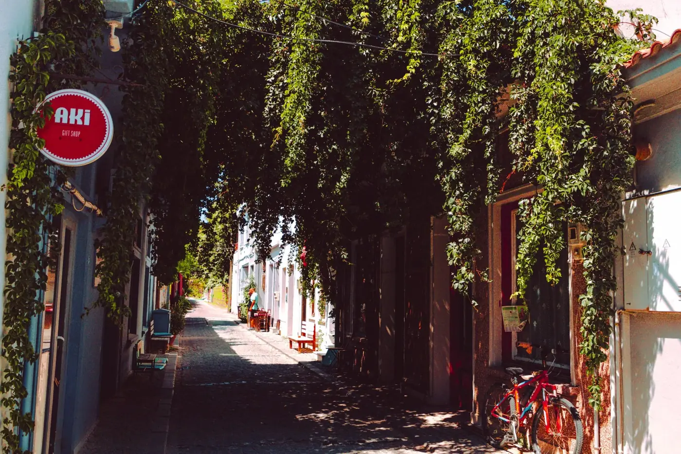 A picturesque narrow alley with lush overhanging foliage and a quaint café sign, perfect for urban exploration.