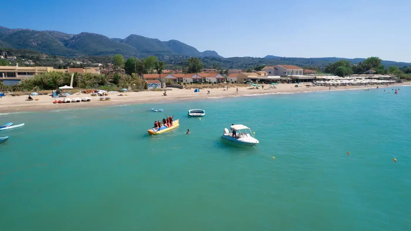 Turquoise sea and vibrant beach scene in Corfu, Greece, capturing summer fun and water activities.