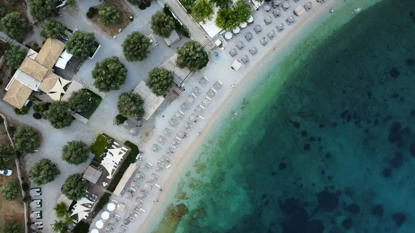 Aerial view of a serene beach in Alonnisos, Greece, with turquoise waters and sun umbrellas.