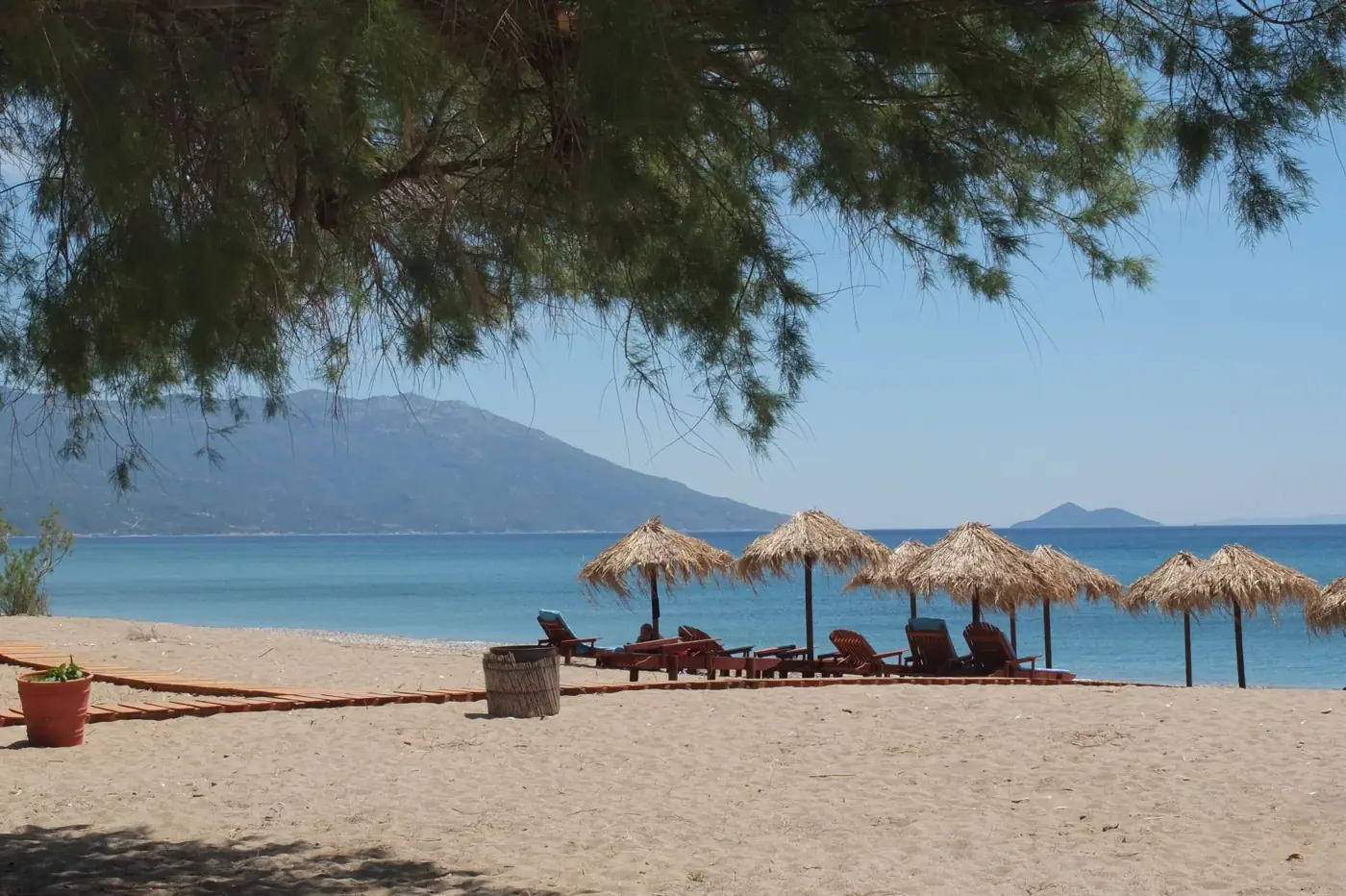 Tranquil beach setting with sunbeds and straw umbrellas under a clear blue sky in Greece.