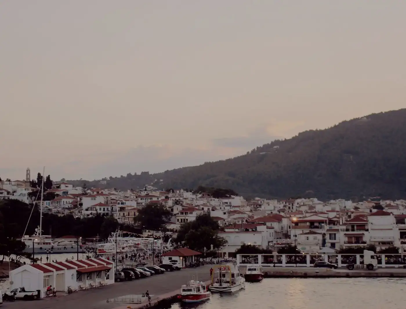 Coastal townscape at sunset featuring moored boats and hillside backdrop.