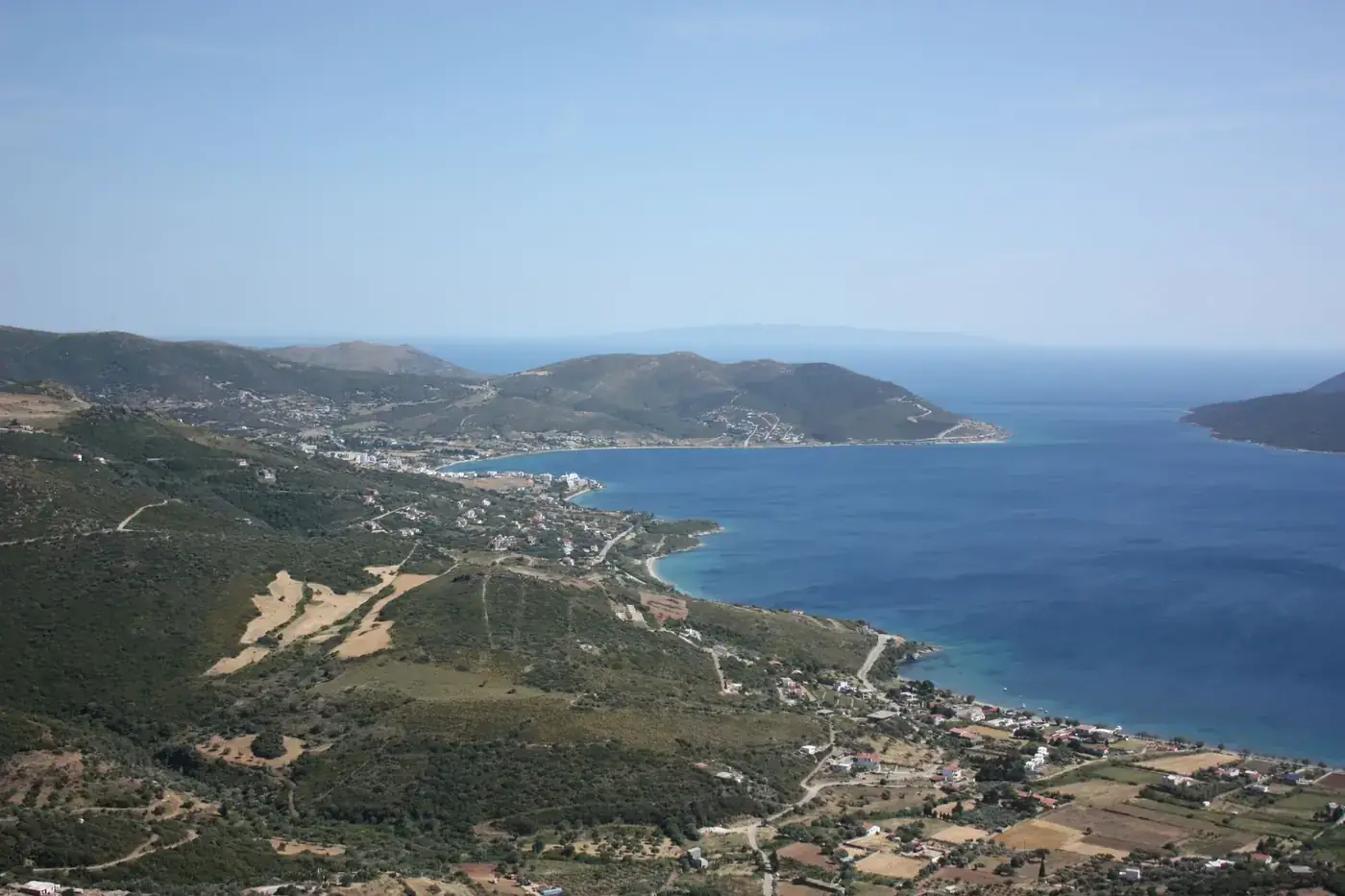 Serene aerial view of a coastal landscape with lush hills and turquoise waters under a clear blue sky.