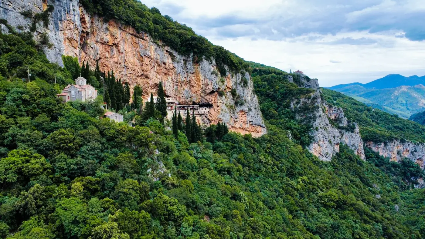 Breathtaking aerial view of a monastery nestled in lush greenery and rocky cliffs in Dimitsana, Greece.