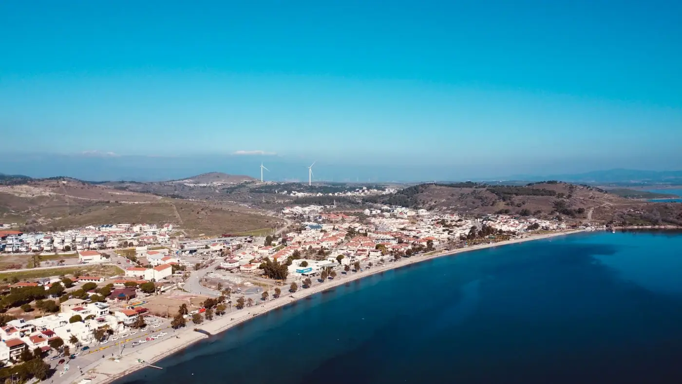 Aerial view of a coastal town by the sea, featuring wind turbines on hills.