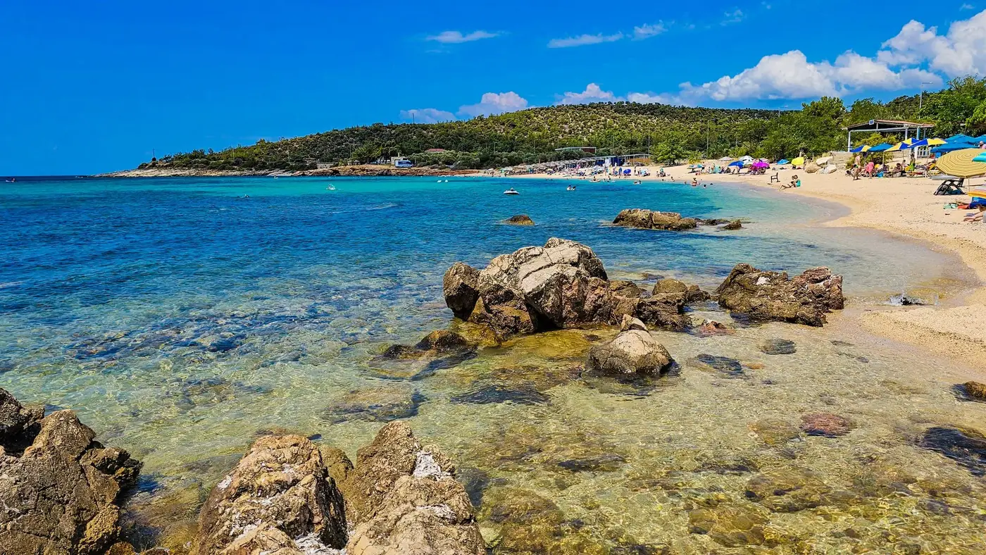 Idyllic beach scene in Thassos, Greece with blue waters and rocky shoreline under a sunny sky.