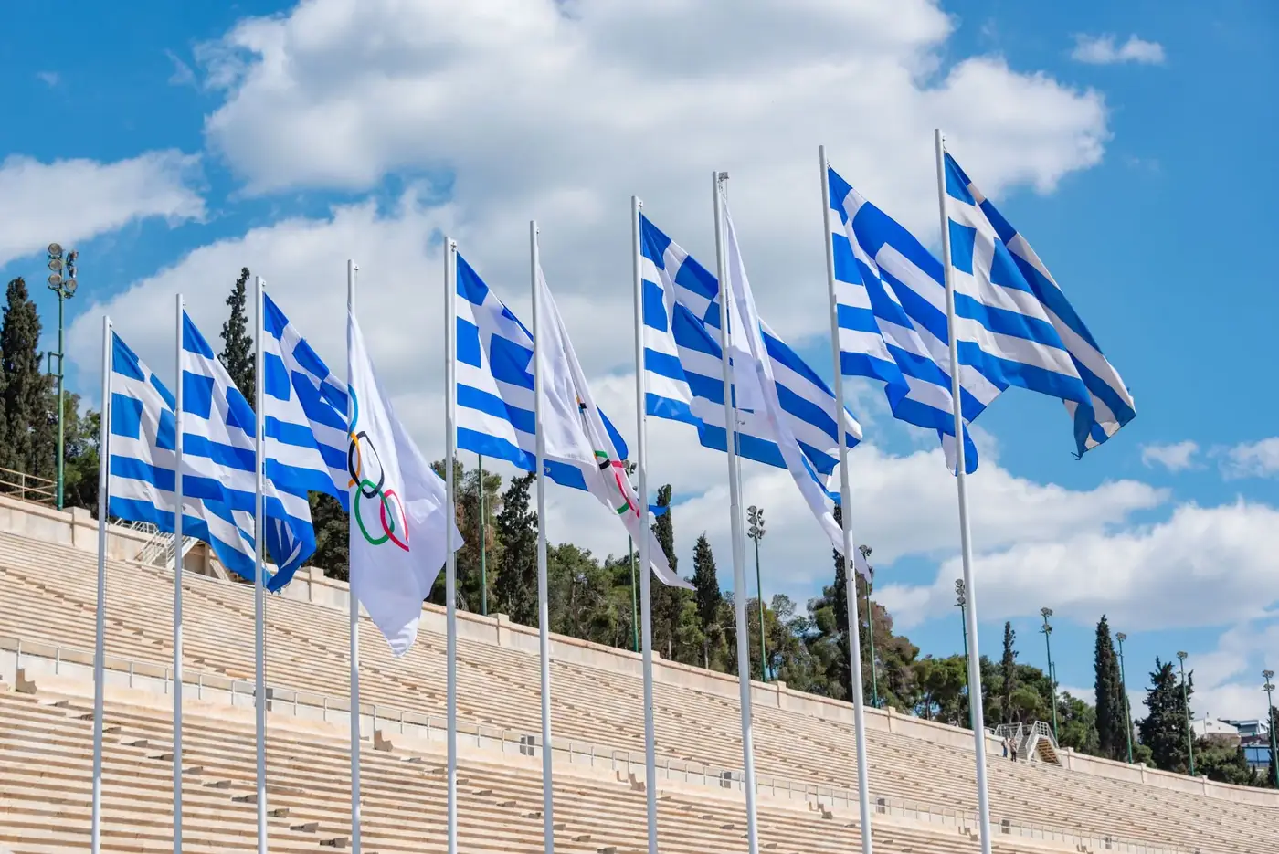 Greek flags waving at Panathenaic Stadium under a clear sky, reflecting Olympic spirit.