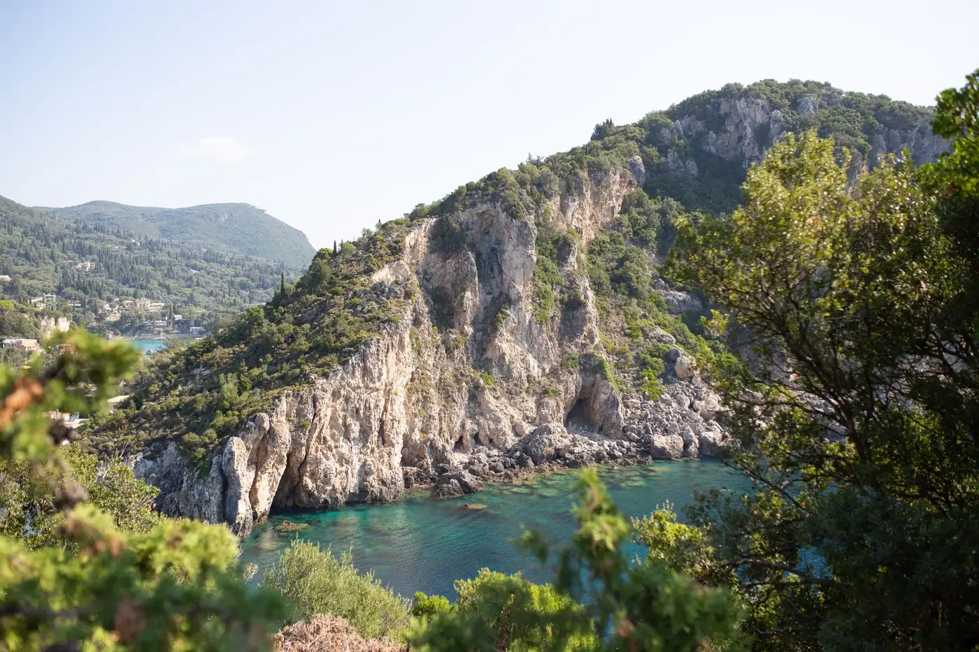 Breathtaking view of a rugged, green coastline with crystal clear waters on a sunny day.