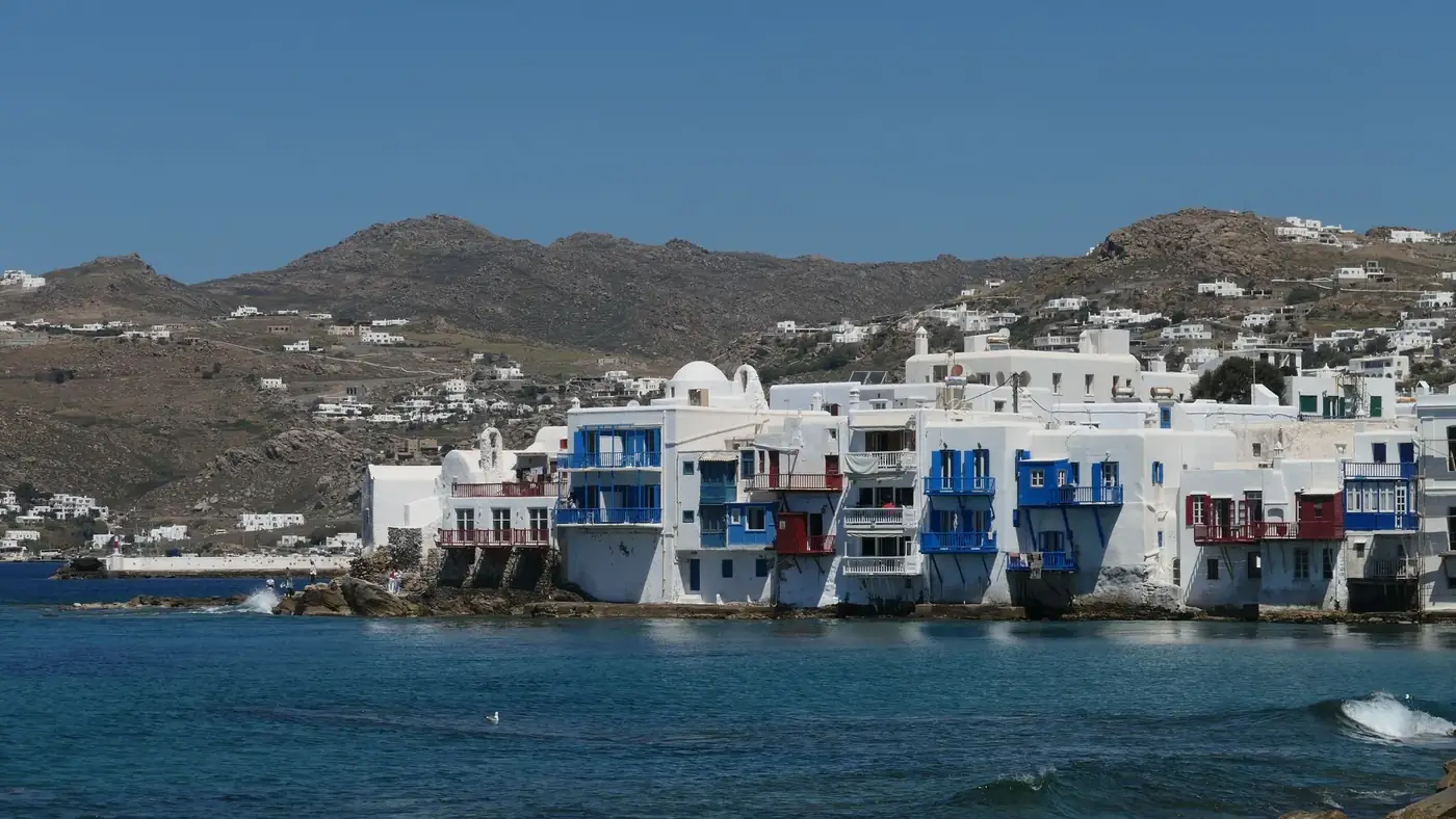 Scenic view of Mykonos waterfront featuring traditional Greek architecture against a mountainous backdrop.