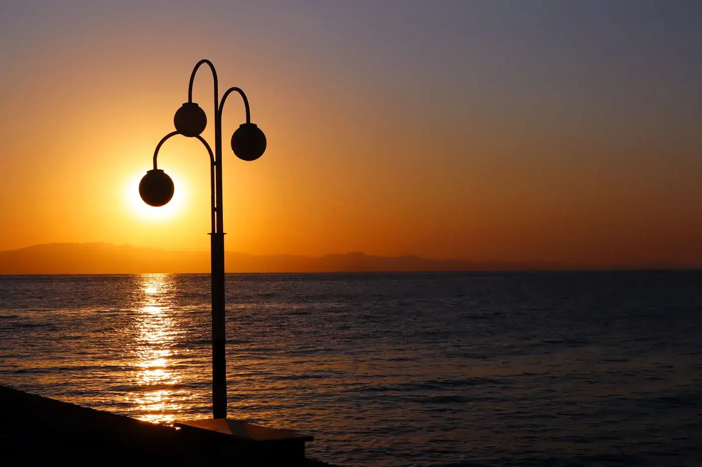 Beautiful sunset over the sea with a streetlight silhouette in Greece. Perfect for travel and nature themes.