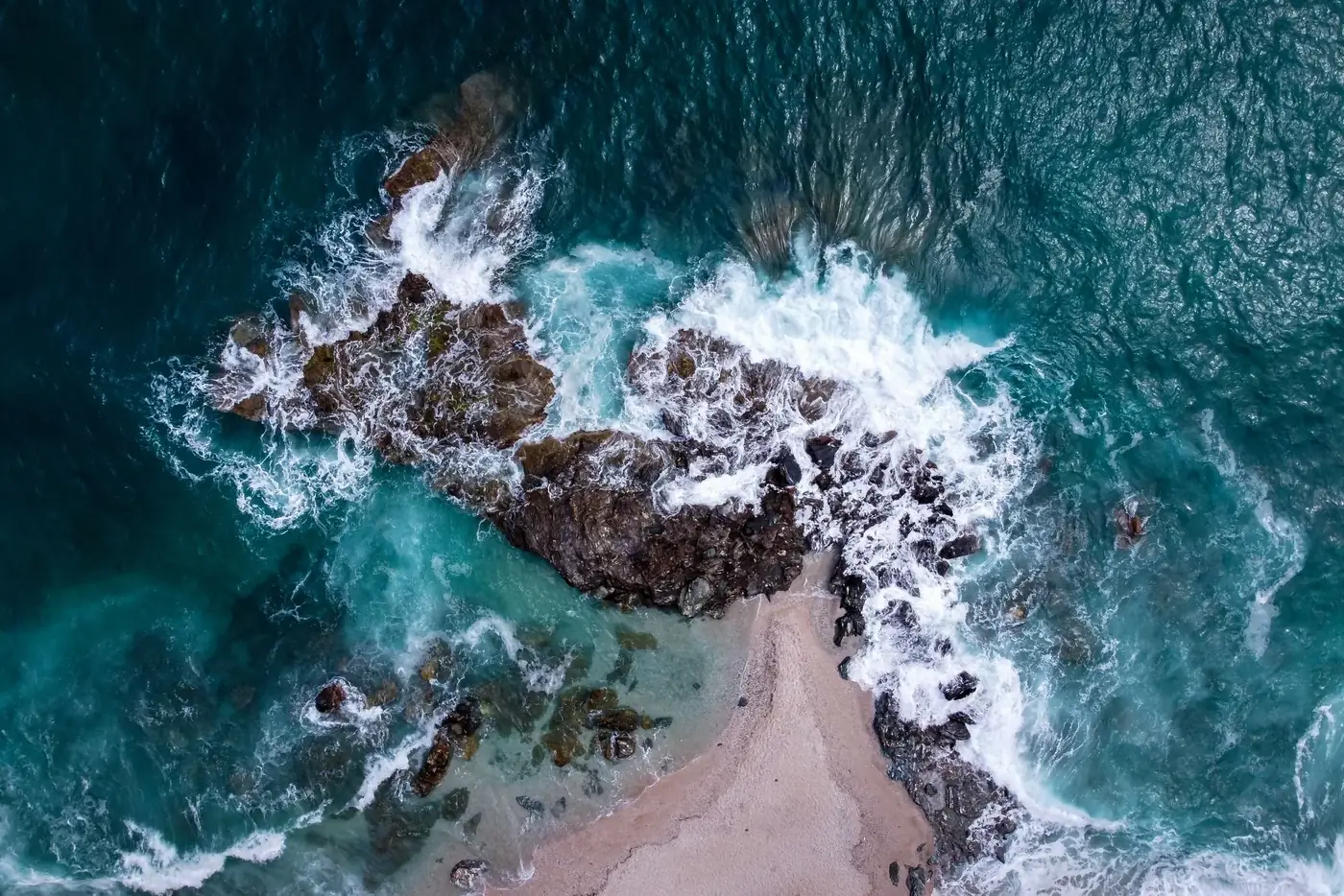 Dramatic aerial view of waves crashing on a rocky Greek coastline.