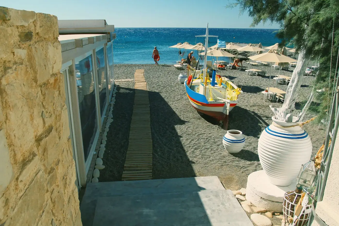 Idyllic beach view featuring a vibrant boat, sun umbrellas, and a clear blue sea.