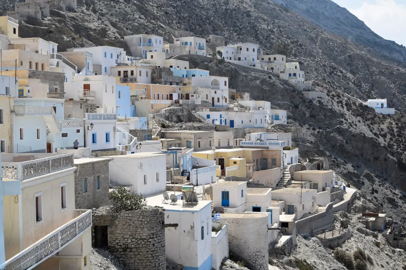 Charming Greek island village with whitewashed houses nestled into a rocky hillside, under a bright sky.