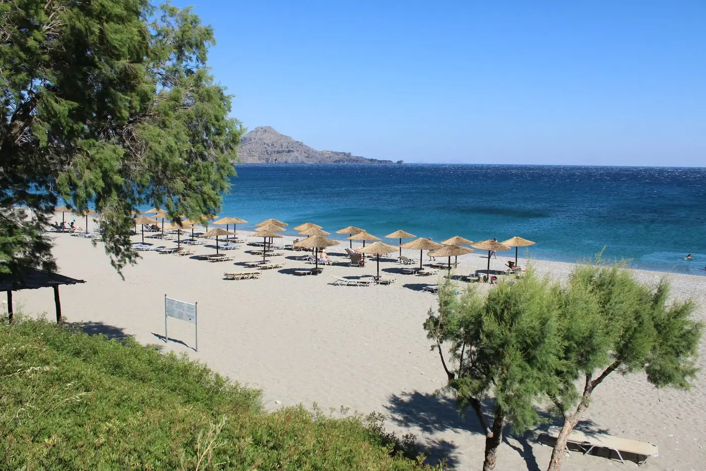 Tranquil sandy beach in Crete, Greece with sun umbrellas and clear blue sea.