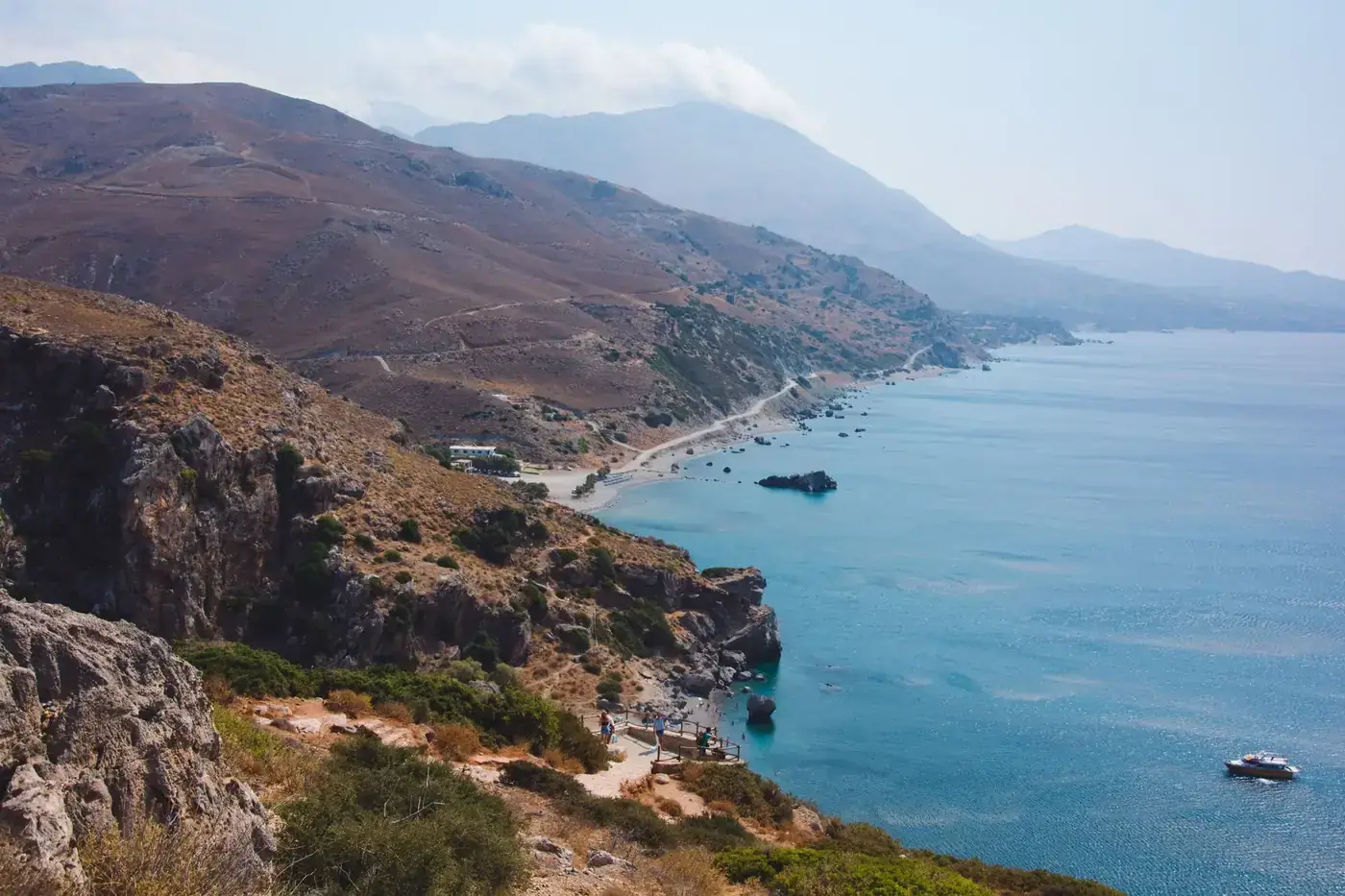 From above magnificent view of blue ocean with sailing ship surrounded by rough sandy ridge with growing grass under ser