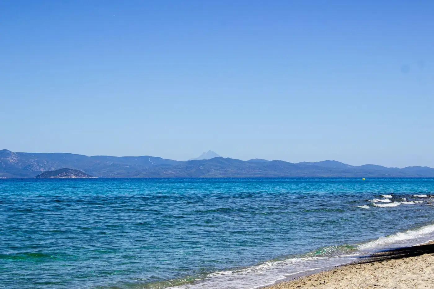 Stunning beach view in Greece showcasing clear blue waters and distant mountains.