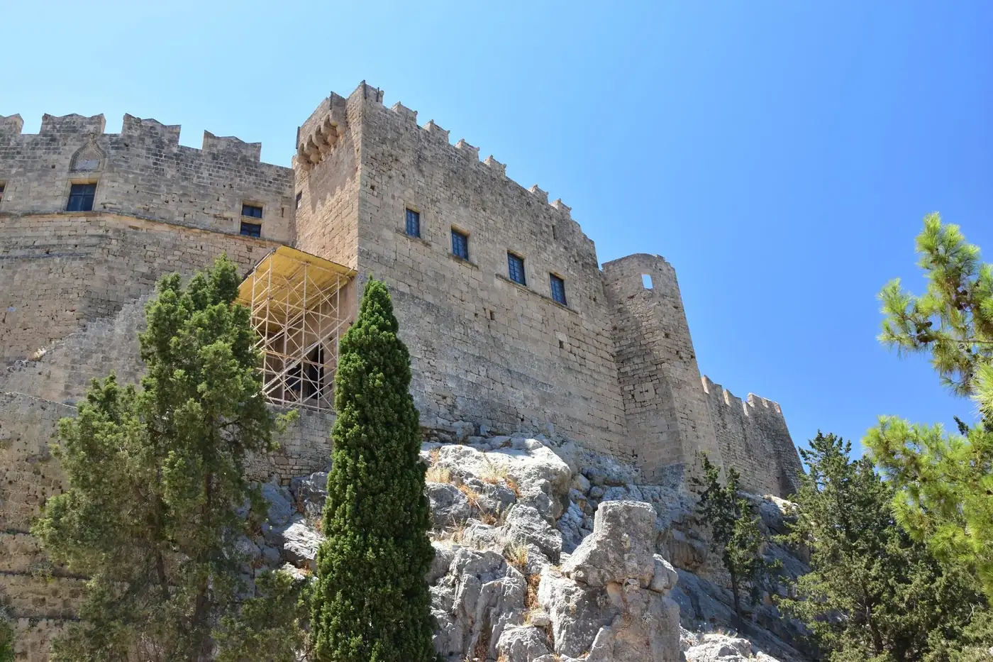 A majestic medieval stone fortress set against a vivid blue sky, surrounded by lush trees.