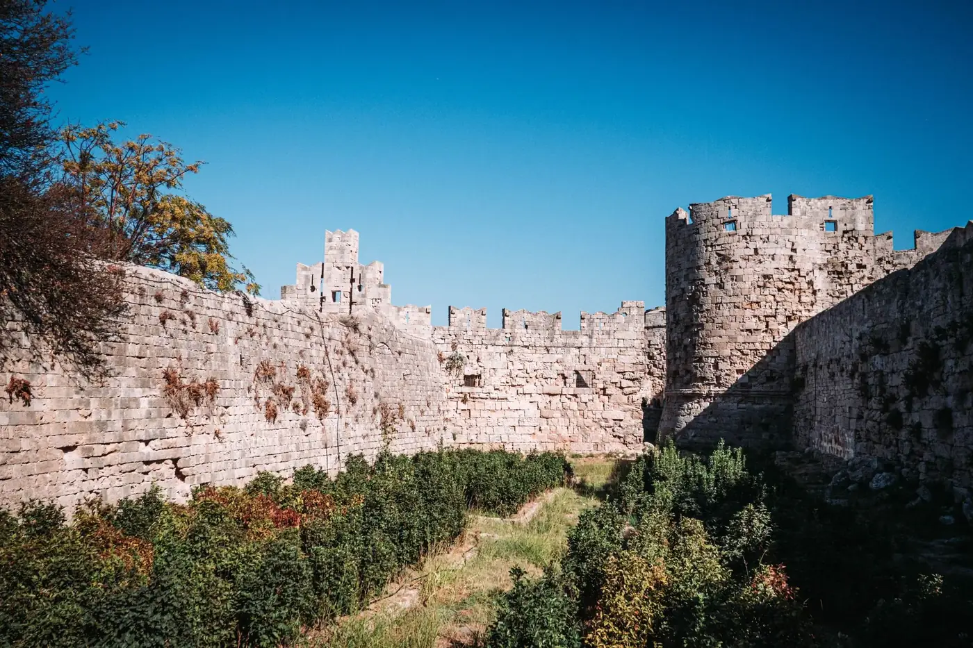 Explore the ancient stone walls of the medieval castle in Rhodes, Greece under a bright blue sky.