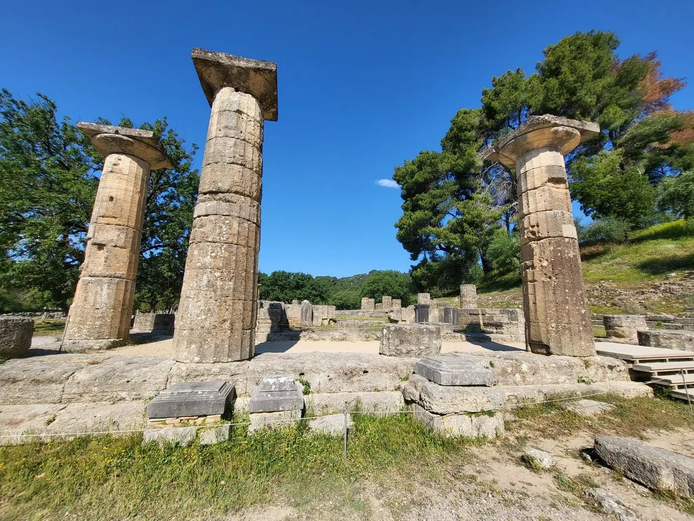 Explore the historic ruins of Olympia, Greece, showcasing well-preserved ancient columns surrounded by lush greenery and