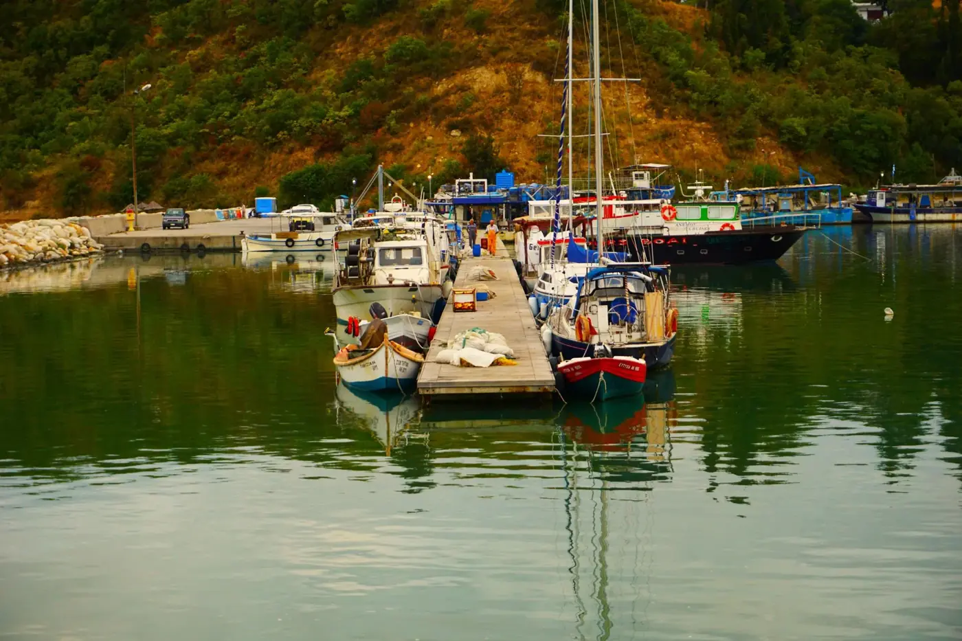 Peaceful scene of boats docked at the pier in Methoni, Greece surrounded by lush hills.