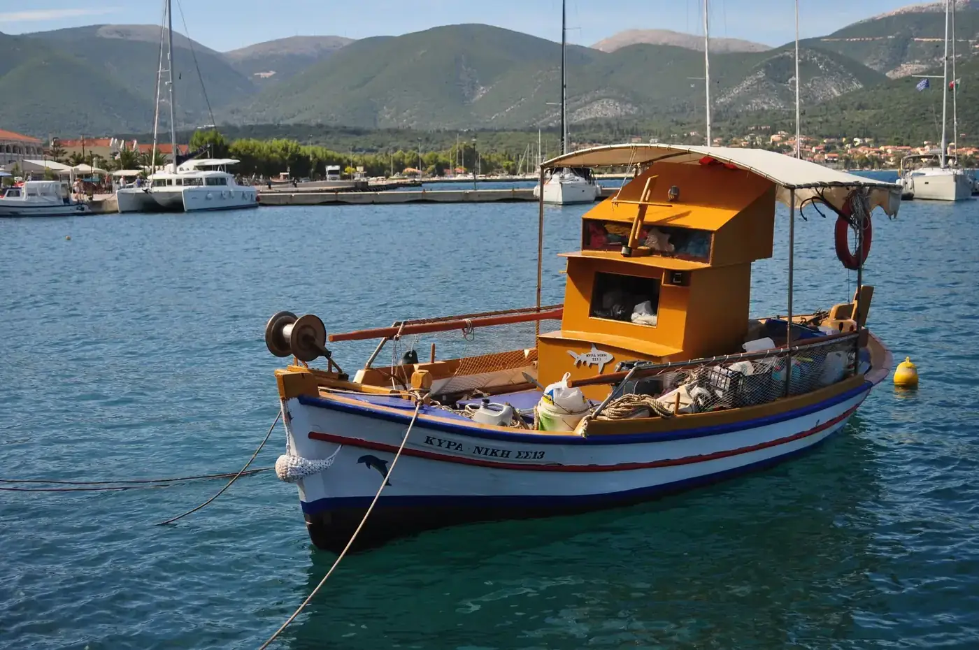 A traditional fishing boat moored in a calm harbor with scenic mountain backdrop.