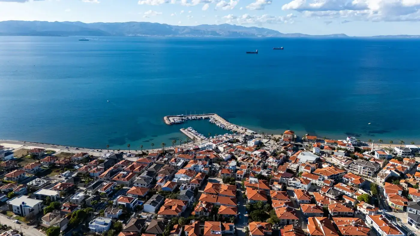 Scenic aerial view of a coastal village with a marina and blue sea under clear skies.