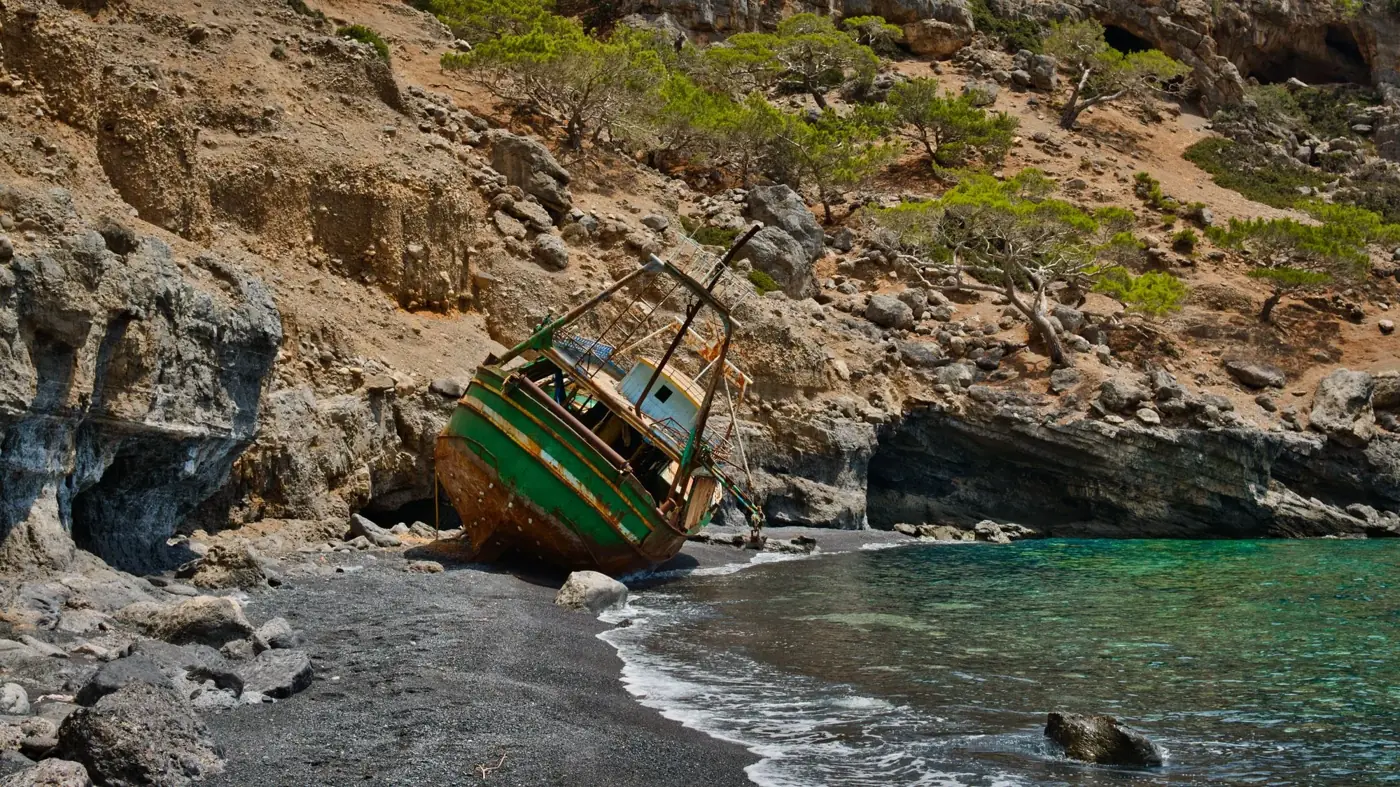 Rustic sunken ship on black sand beach in Rethymno, Greece at daytime.