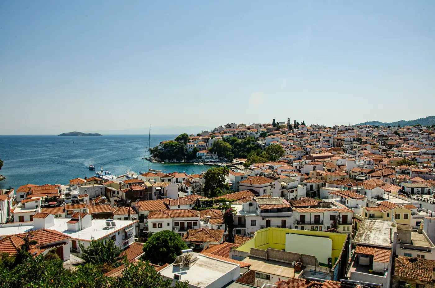 A picturesque coastal village with red-tile roofs overlooking the serene sea under a clear blue sky.