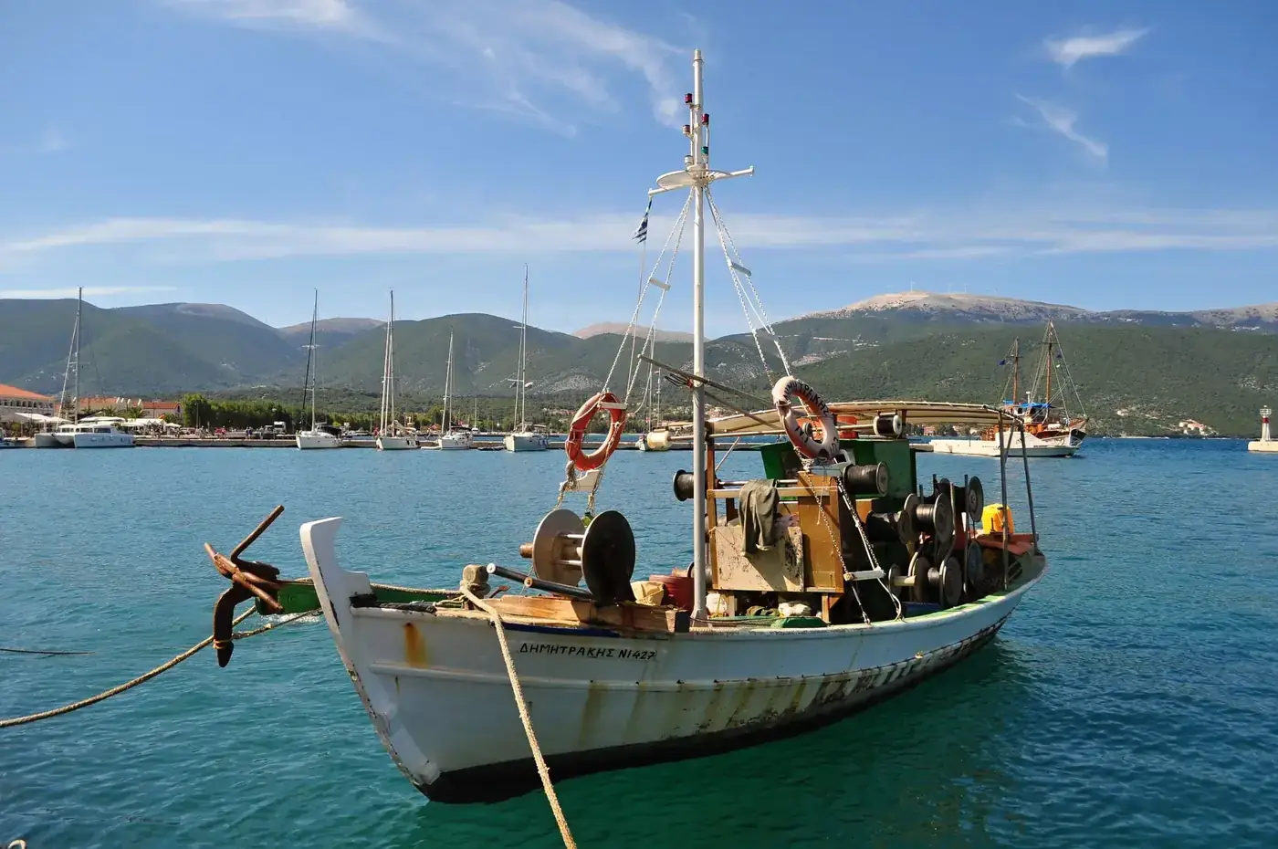 A traditional fishing boat docked in a scenic coastal Greek harbor with mountains.