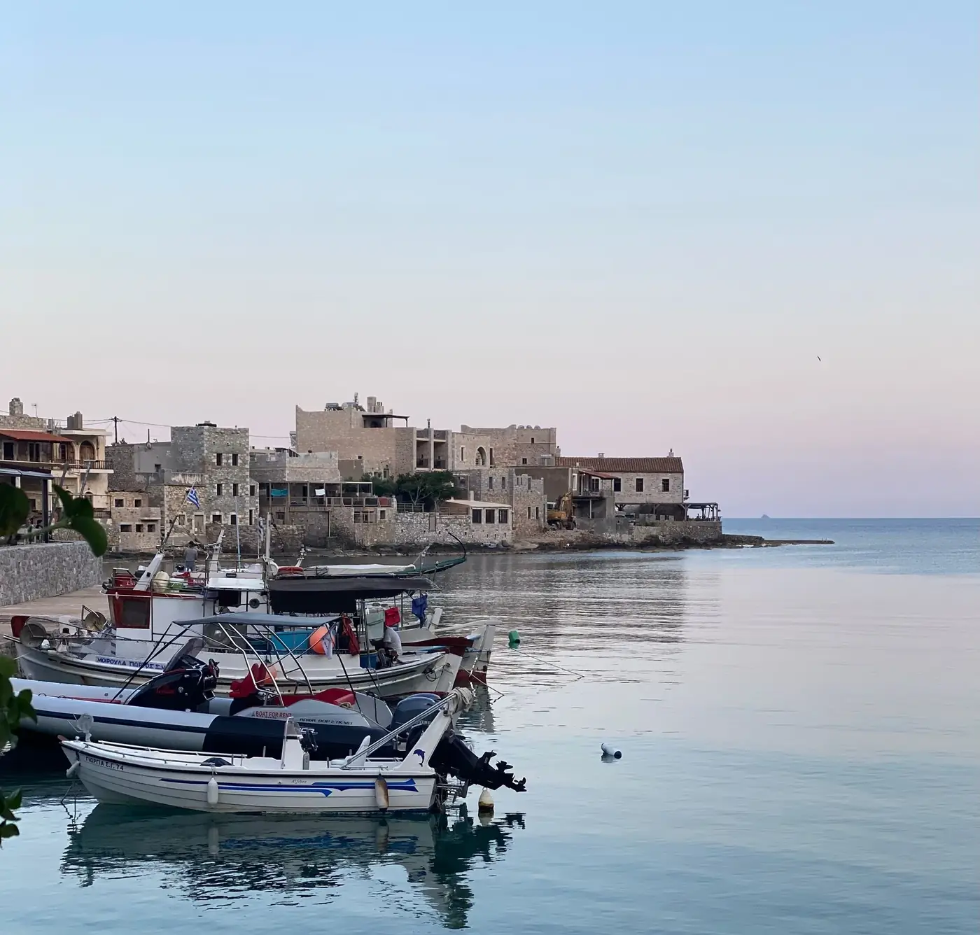 Charming view of Gerolimenas harbor with boats and stone buildings at twilight.