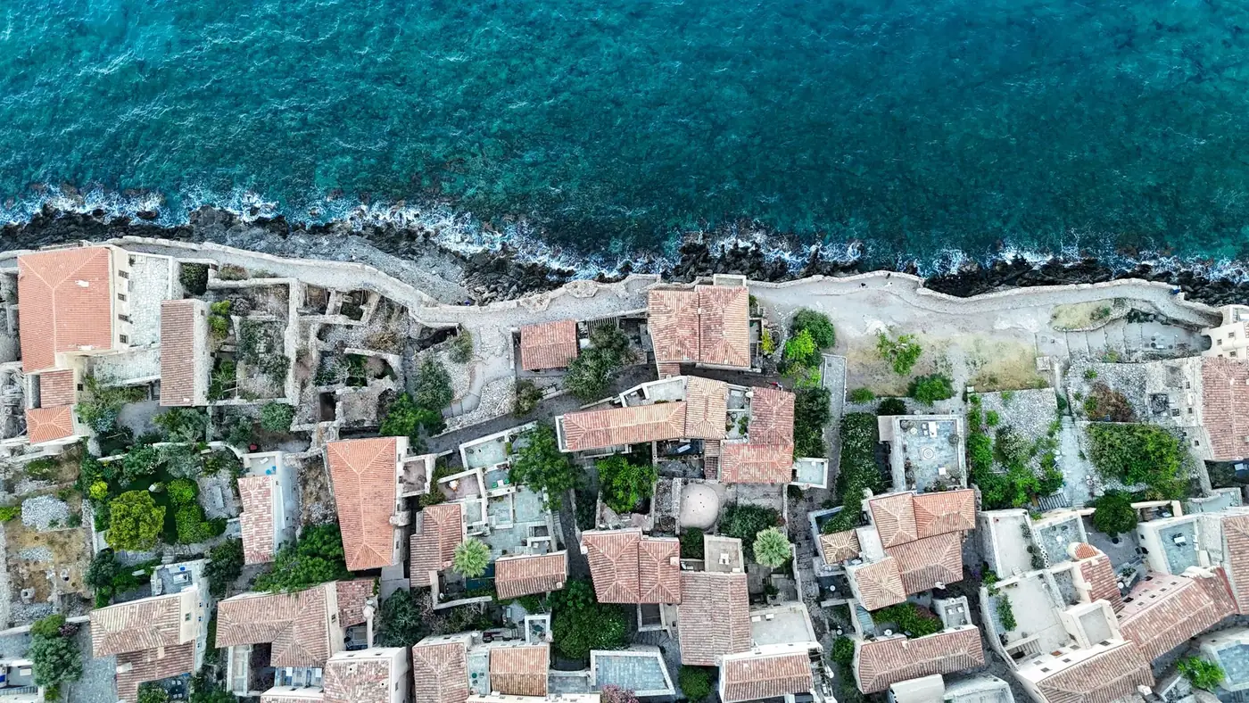Stunning aerial shot of the coastal city Μονεμβασιά, Greece showcasing traditional architecture and the vibrant sea.