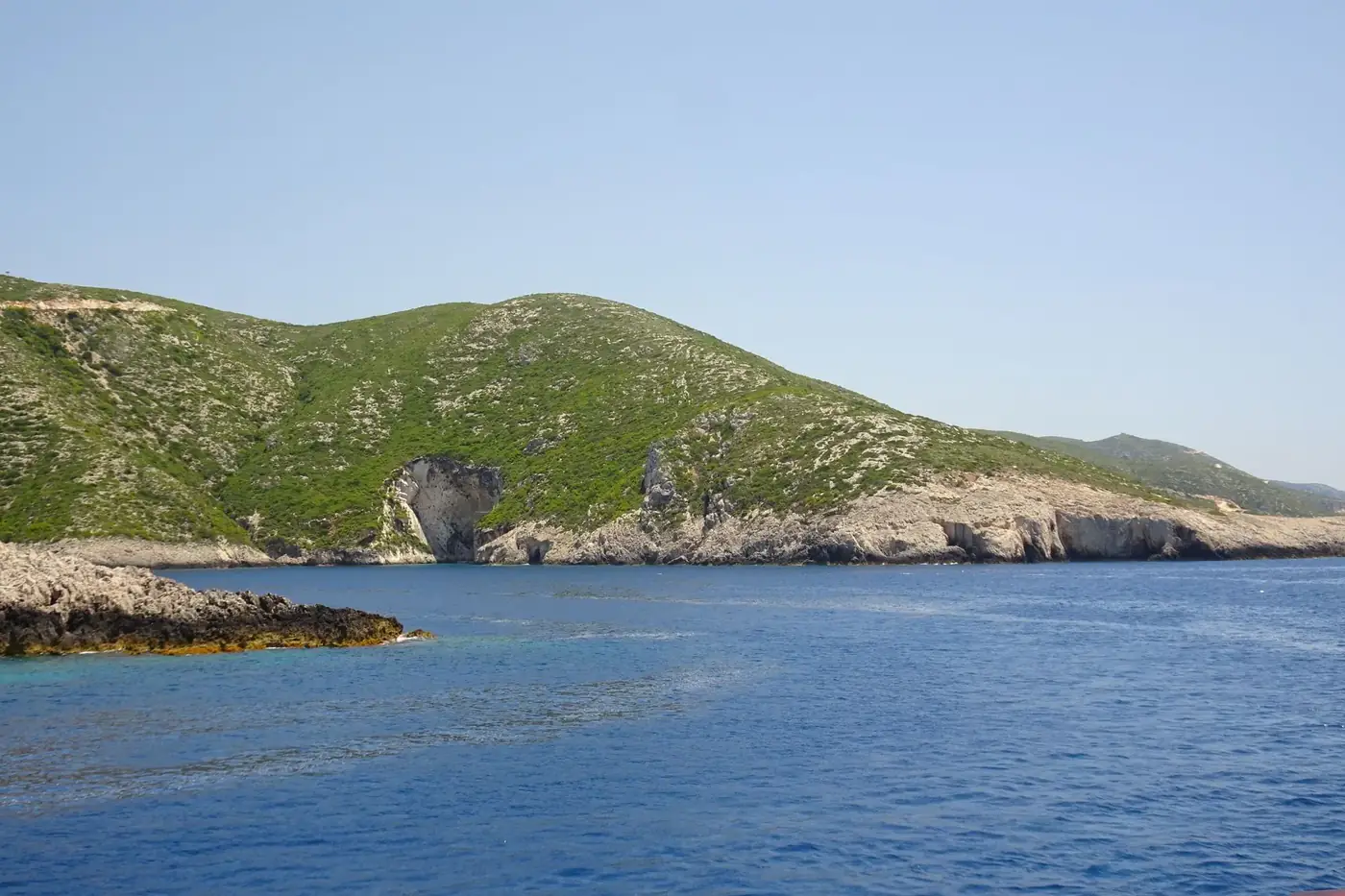 Captivating view of a rocky coastline with lush hills by the blue sea in Greece.