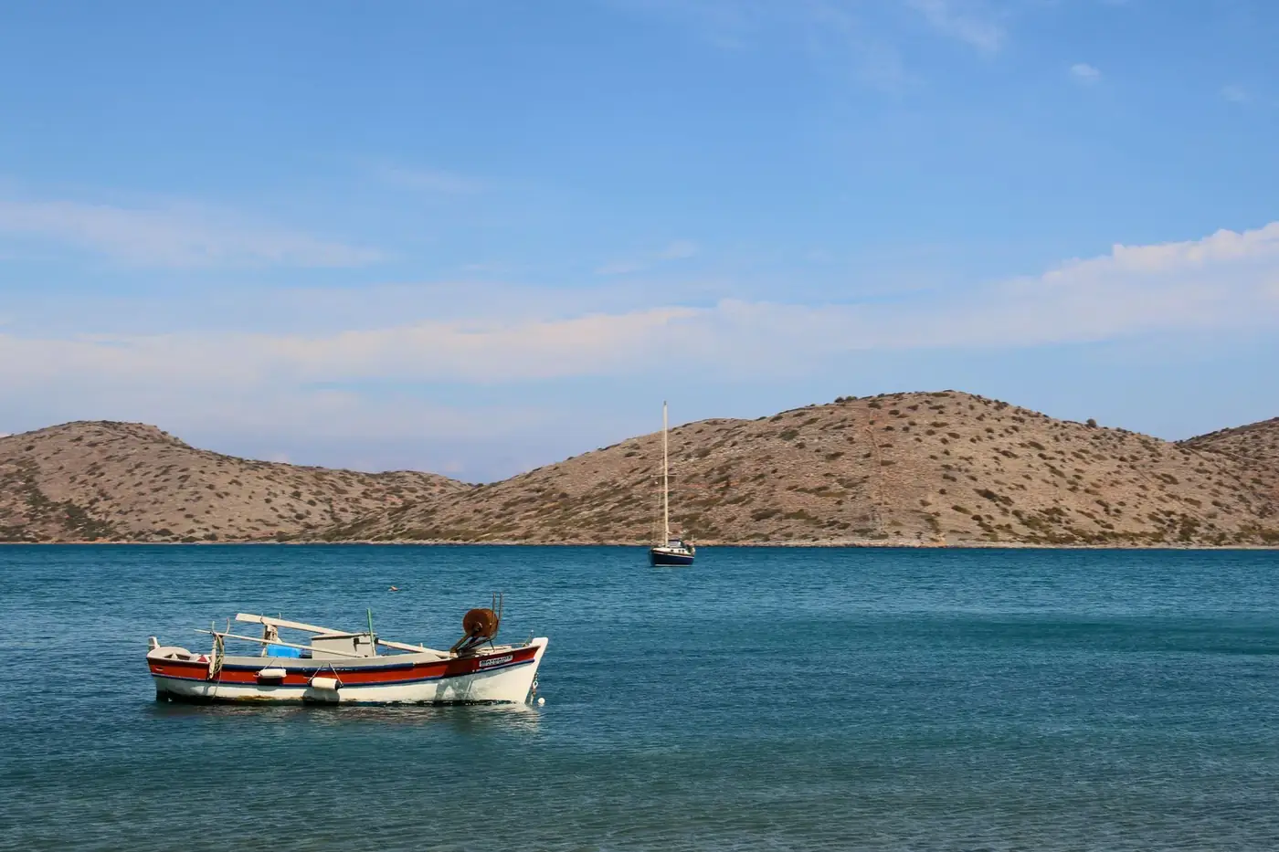 Peaceful scene of fishing boats on the Aegean Sea with Greek islands in the background.