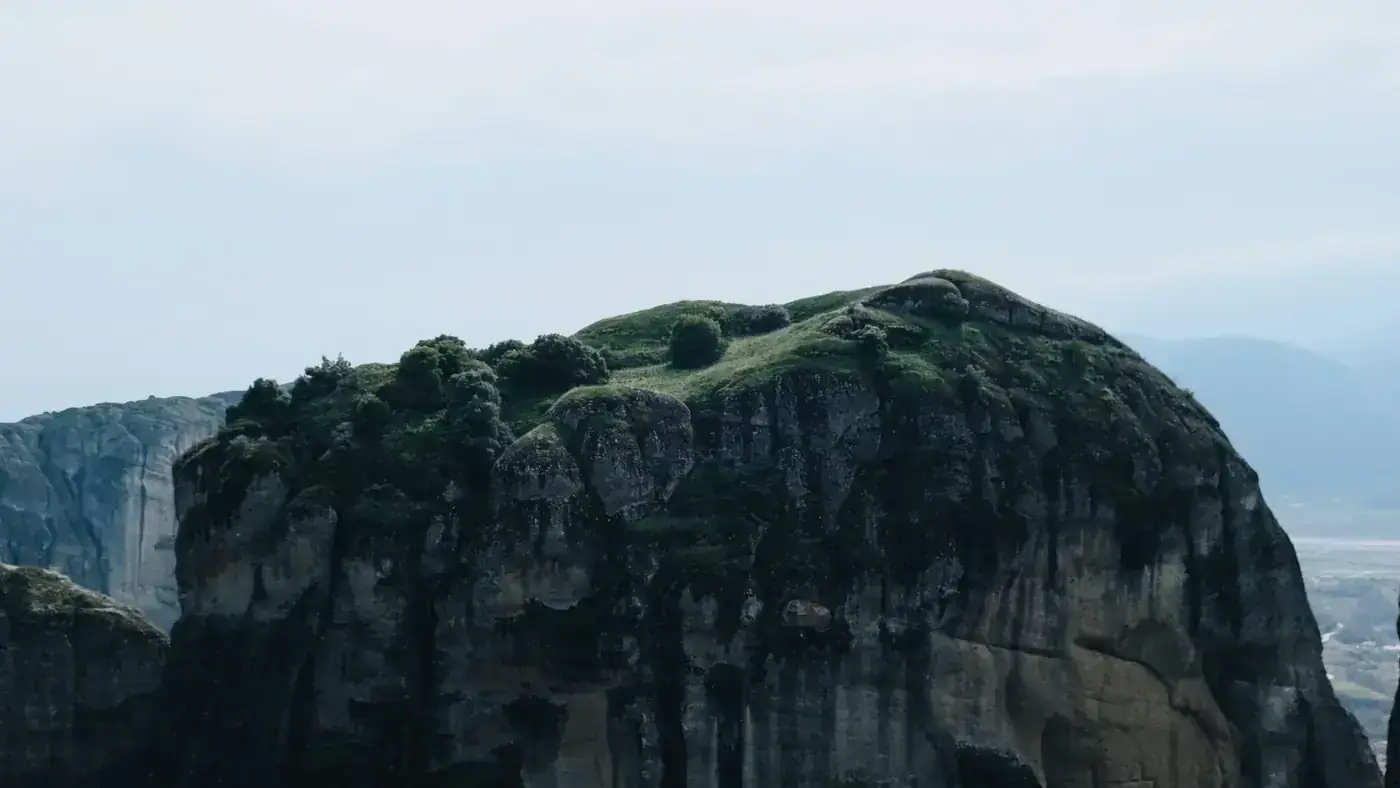 A stunning cliff with lush vegetation under a serene sky, showcasing natural beauty.