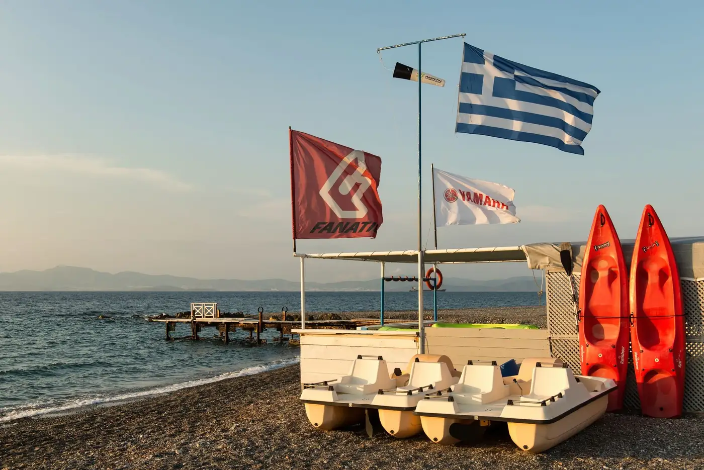 Tranquil beach scene on Kos island featuring paddle boats and Greek flags, ideal for tourism imagery.