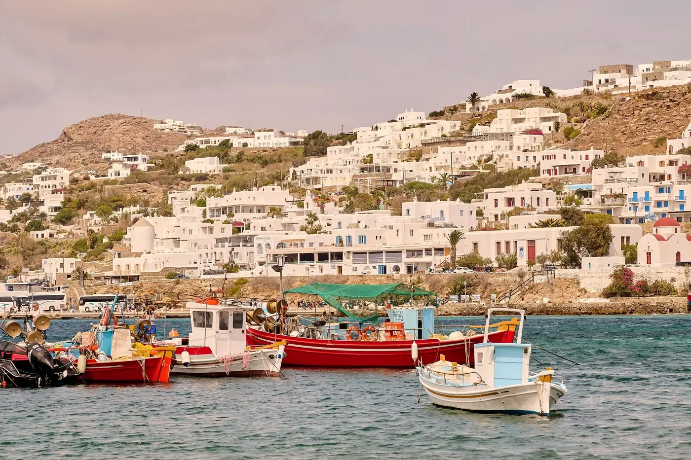 Charming white buildings and vibrant boats in Mykonos harbor on a sunny summer day.