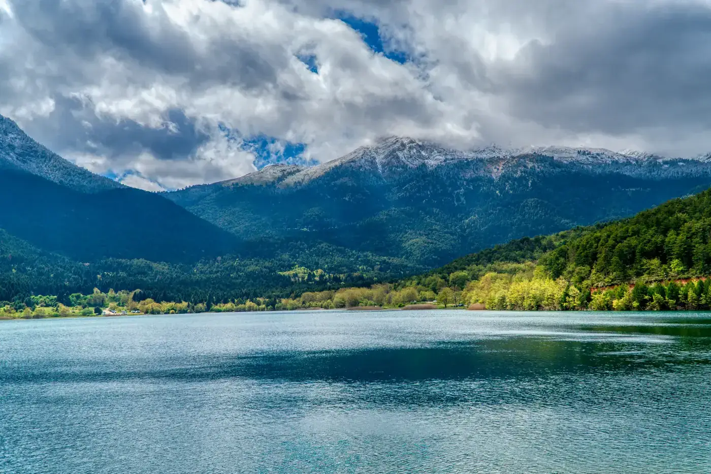Peaceful landscape of Lake Doxa surrounded by lush greenery and majestic mountains in Greece.
