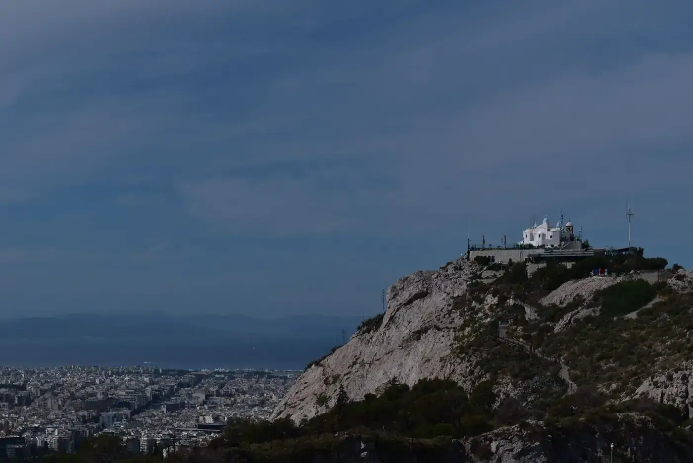 A wide view of Mount Lycabettus with Athens cityscape below, featuring distinct limestone formations and a prominent cha